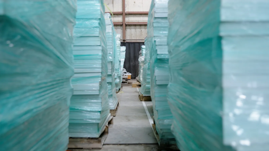 Several rows of solar panels wrapped in blue plastic are stacked high on pallets