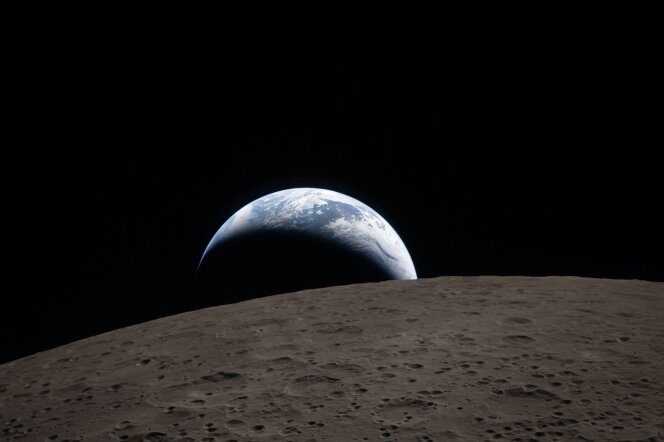A third of the planet earth set against a pitch black sky. In the foreground is the brown, cratered surface of the moon.