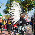Dancers perform Danza Azteca outside, with one person wearing a white and black-colored outfit.