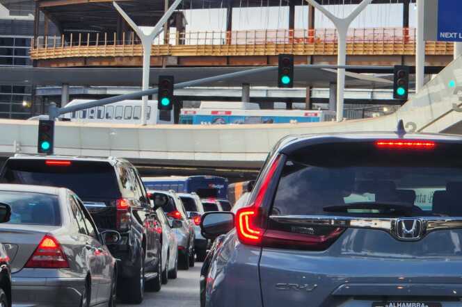 Dozens of cars in two rows fill the roads at the LAX airport. In the from of them is construction for the airport train.