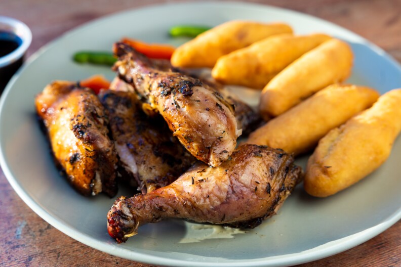 A plate of jerk chicken with its dark grilled edges next to fried bread