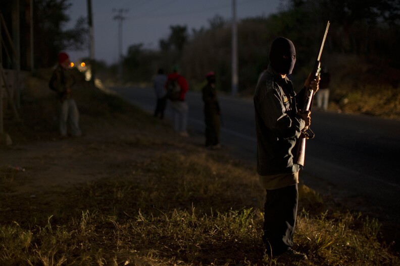 An armed and masked man guards a roadblock at the entrance to the community of Cruz Quemada, near Ayutla, early Saturday, Jan. 19, 2013. Hundreds of  men in the southern Mexico state of Guerrero have taken up arms to defend their villages against drug gangs, a vigilante movement born of frustration at extortion, killings and kidnappings in a region wracked by violence.  