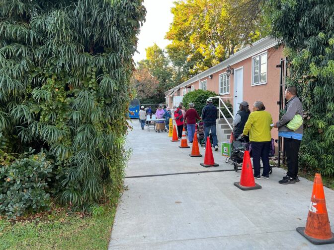 A line of people lining up along a driveway next to a peach color building.