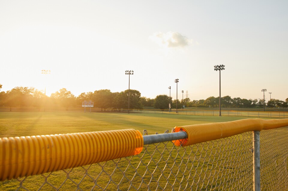 A chain link fence with an orange protective coil on top marks the edge of a lighted playing field.