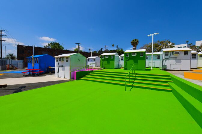 a tiny home village of about 11 homes is shown. Some of the homes are painted green, one is blue.
