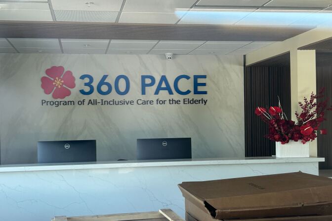 The interior of a business in transition — packing boxes are lined up, but there are welcoming flowers in the reception areas and computer monitors. Signage reads: "360 PACE Program of All-Inclusive Care for the Elderly"