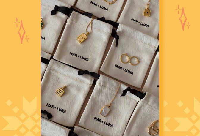 Rows of small cloth sacks with words Mar + Luna printed on them with gold lockets and rings placed on top.