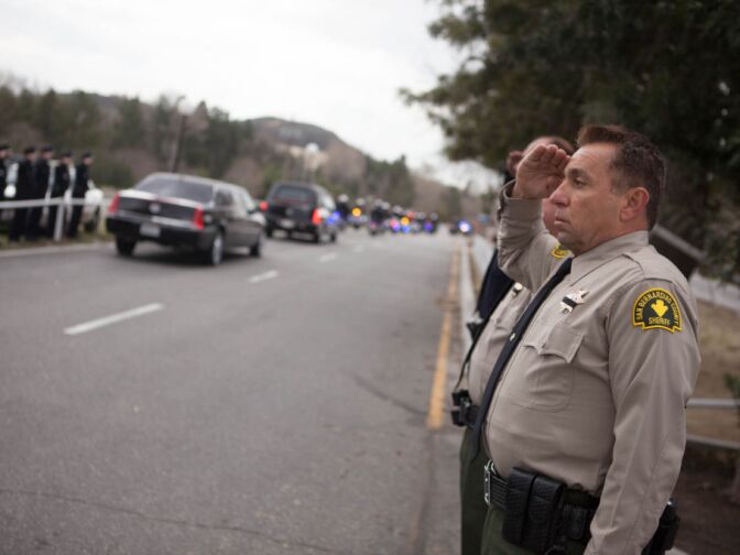 A San Bernardino Sheriff's deputy stands at attention as the funeral motorcade for Det. Jeremiah MacKay passes by.