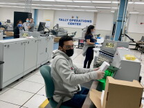 Five people dressed in T-shirts and sweats sit or stand at large scanning machines. 