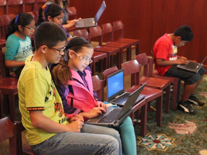 Nathaniel Victoria (first row, left), age 12, shares a computer with his 10-year old sister Sophia (first row, second from left) to complete a tutorial on algorithms