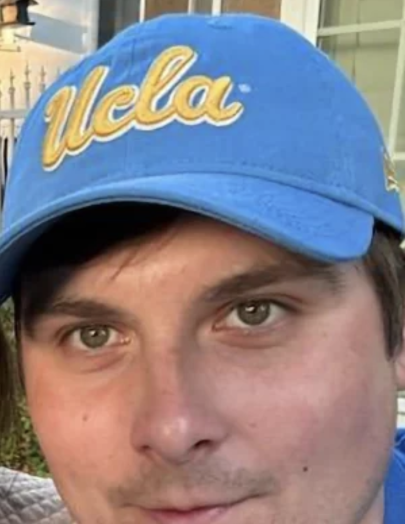 A man with light-tone skin wears a UCLA ballcap. His chin is not visible in the frame.