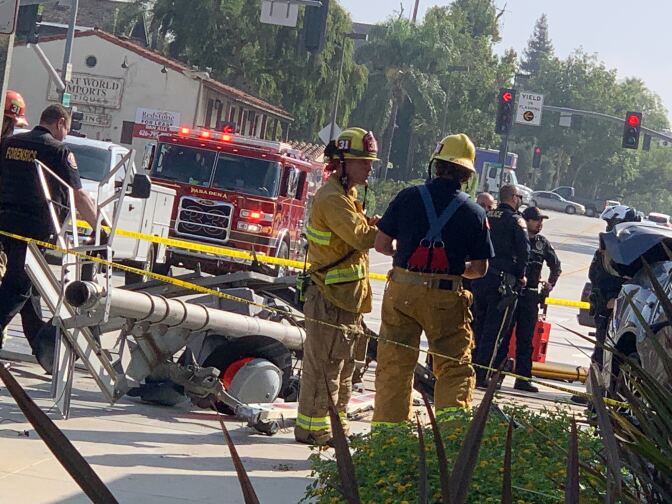 Firefighters stand near a collapsed pole with police tape and a fire truck visible.
