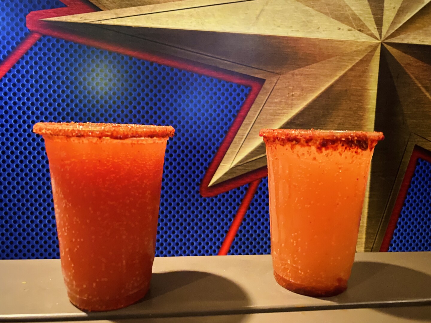 Two plastic cups are filled with orange liquid and rimmed with orange salt.