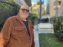 Dave Goldstein, a man with light skin tone, stands at the gate to one of his properties, a 1930s Streamline Moderne building in Hancock Park where John F. Kennedy once lived.  