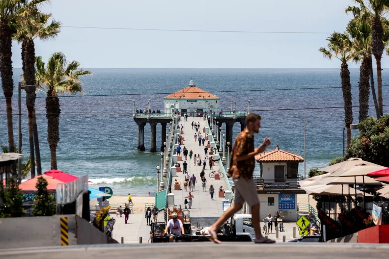 A long concrete boardwalk in the daytime over a blue ocean. It is full of people walking and biking.