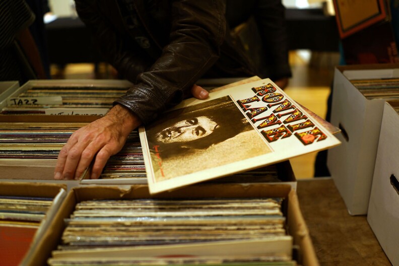 A person's hand is seen searching through boxes of albums