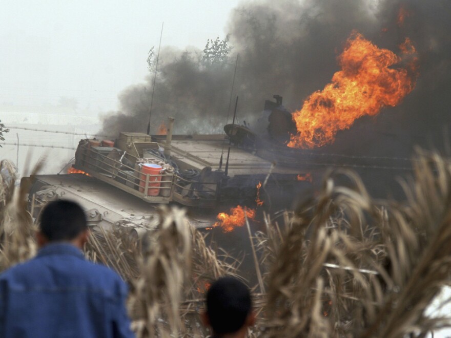 Iraqis look at a burning U.S. Army Abrams battle tank on March 10, 2006, after an IED exploded on a highway in eastern Baghdad.