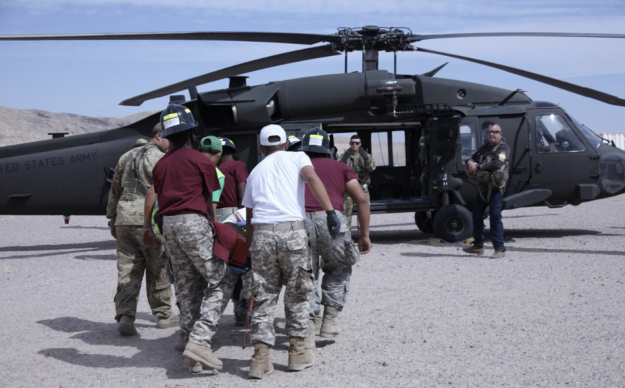 A group of medics wearing camo pants simulate taking a patient into a helicopter during an NVMI Summer Camp.