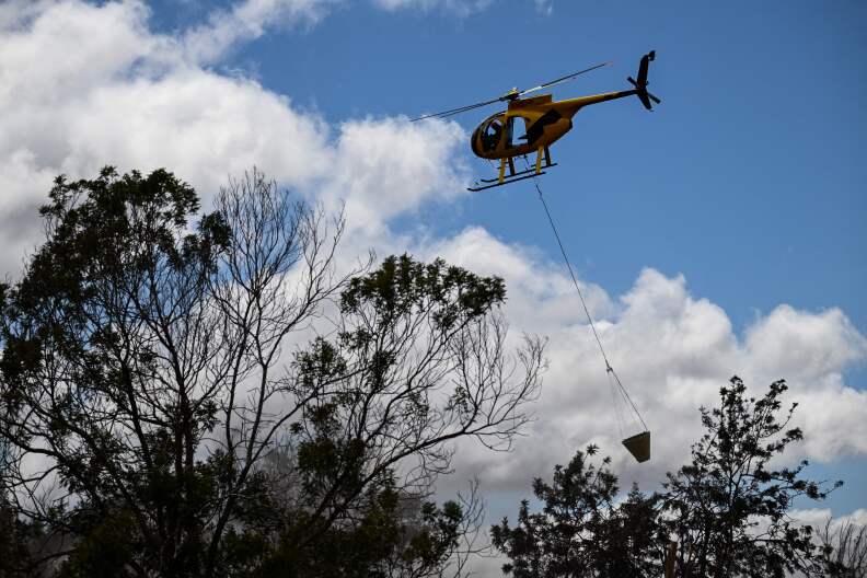 A firefighting helicopter drops water as Maui County firefighters extinguish a fire near homes during the upcountry Maui wildfires in Kula, Hawaii on Aug. 13, 2023.