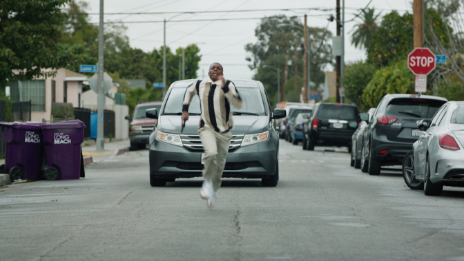 A man shows down the middle of the street as a car chases him.