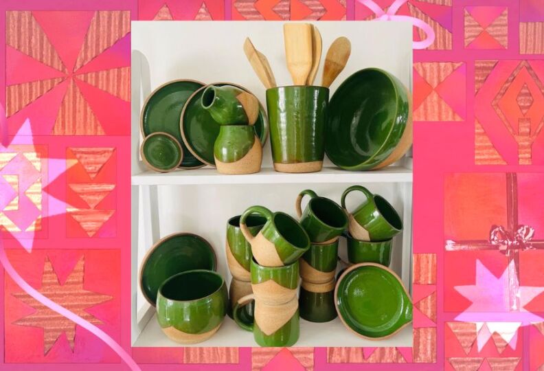A photograph of a ceramics collection of kitchen items: There are bowls large and small, cups, mugs, saucers and a holder for wooden utensils. The pottery is made out of taupe, earthy clay and then finished off with a vibrant green glaze. The photograph is set against a decorative pink background accented with stars, gift boxes and strands of ribbon.