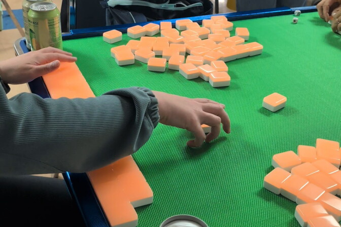 A hand reaching for a Chinese mahjong game tile on top of a table.