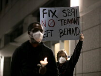 A masked protester holds up a sign reading Fix SB91 No Tenant Left Behind