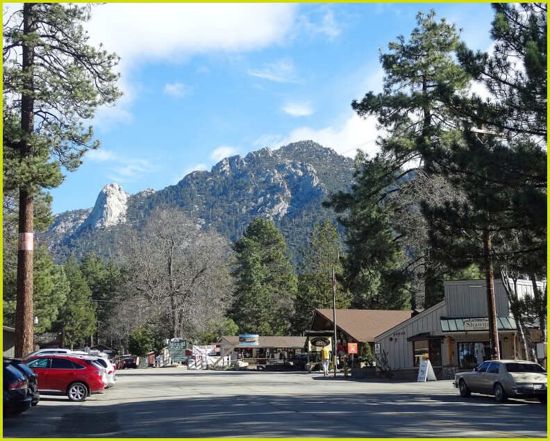 A small town square with businesses and in the background there are mountains with snow.