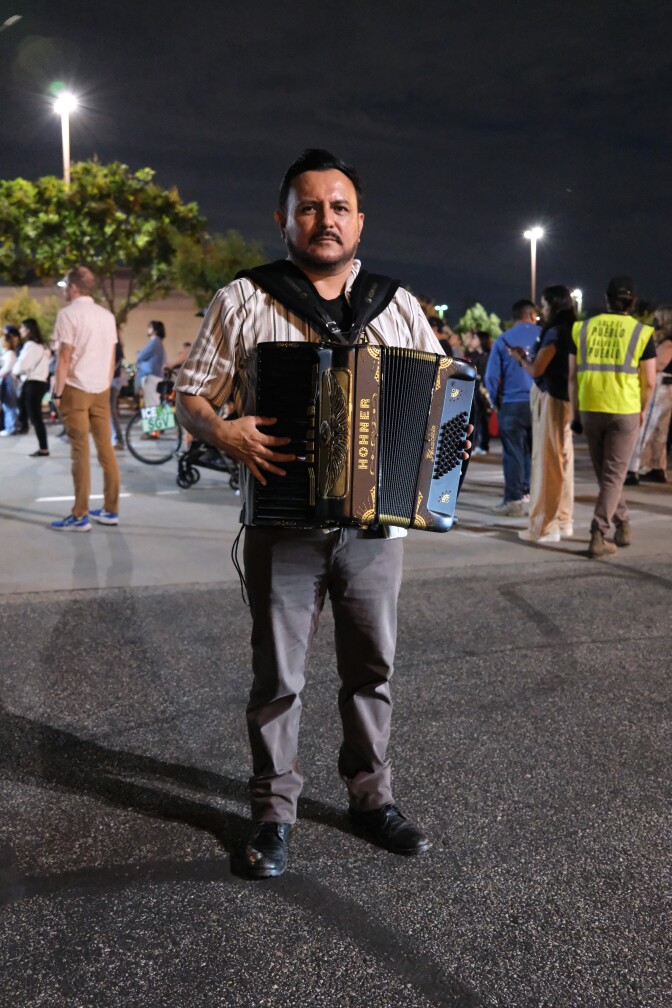 A man holds an accordion while standing in a road at night.