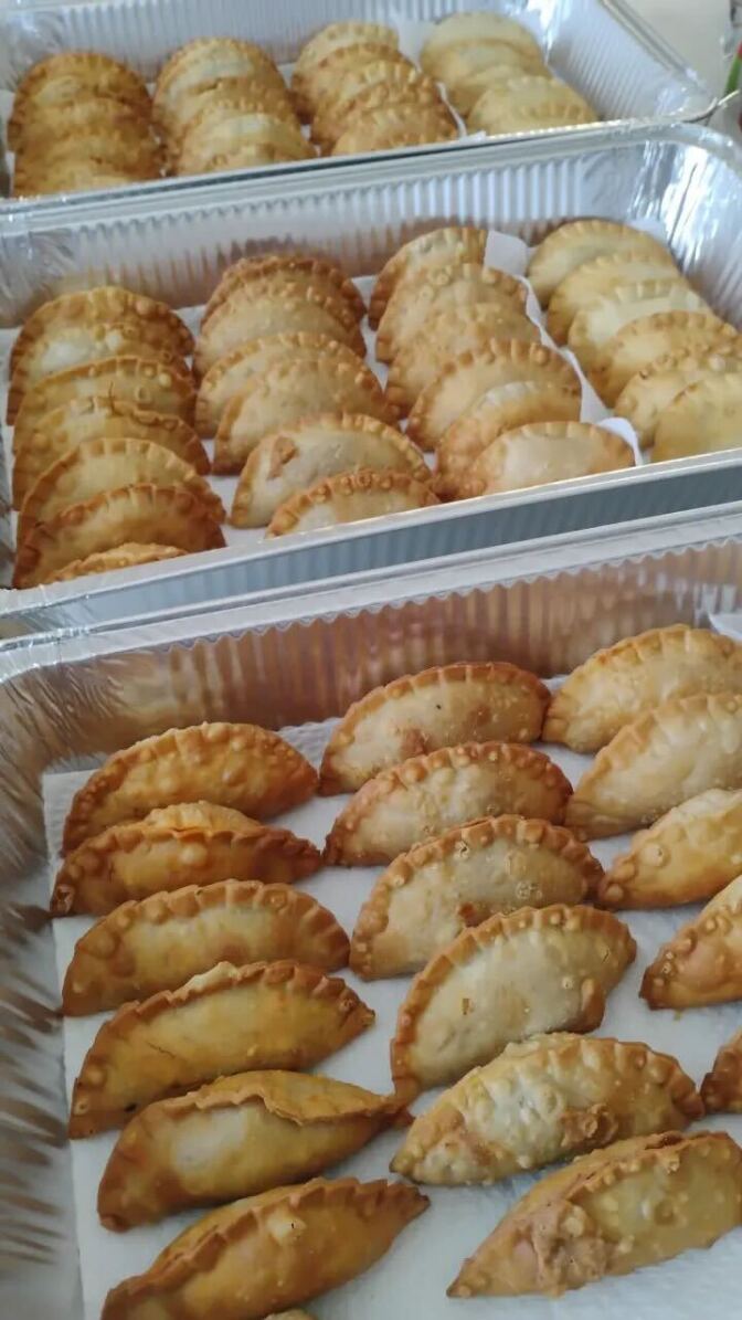 Several rows of golden fried empanadas arranged in an aluminum catering tray lined with parchment paper.