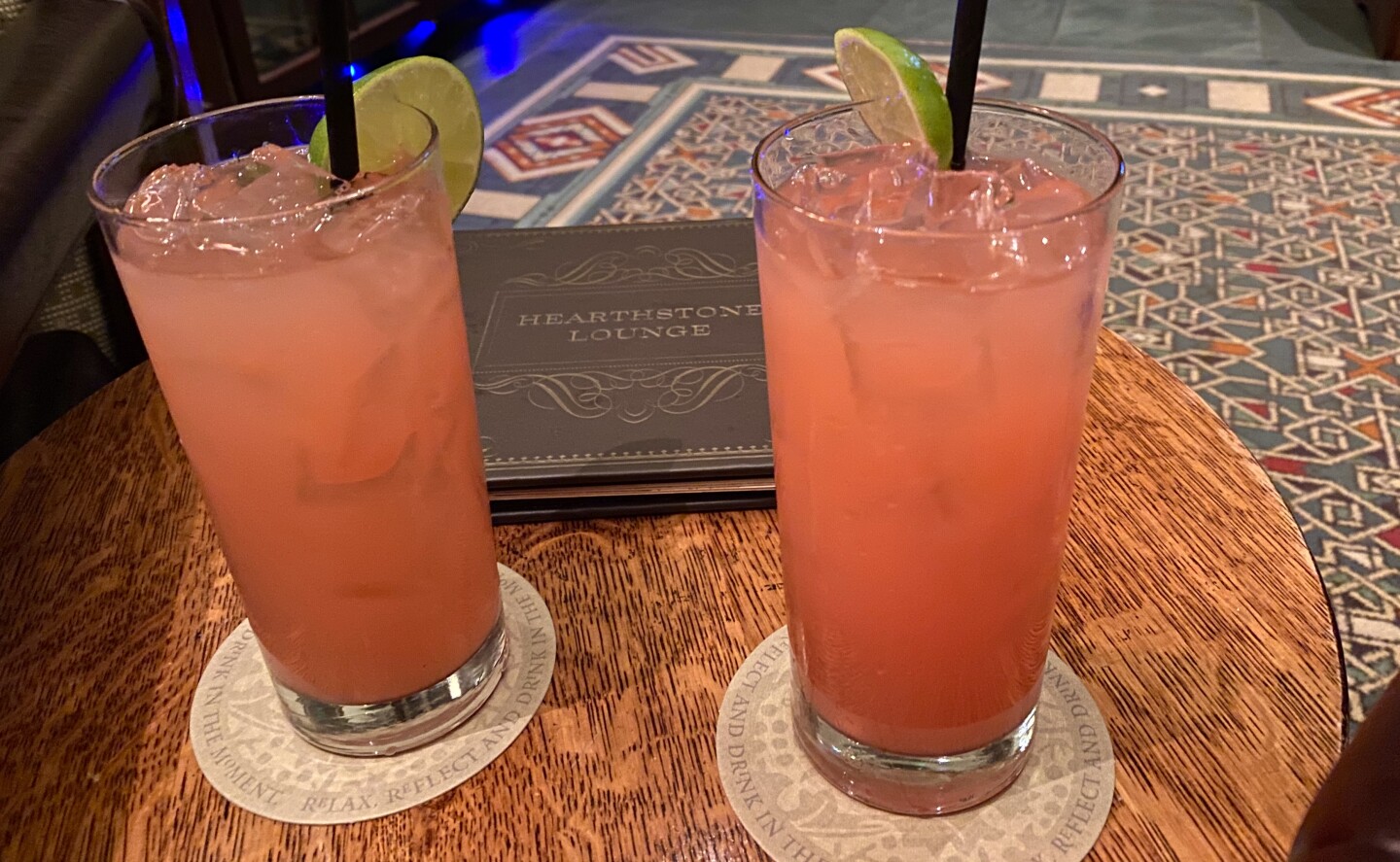 Two tall glasses are filled with pink liquid. They sit on a round wooden table.