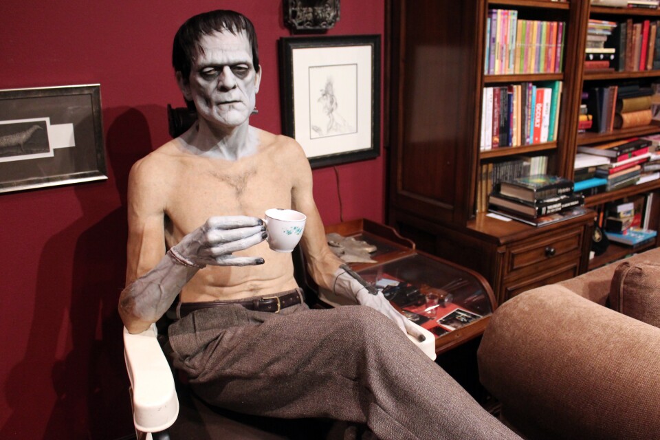 A life-size Frankenstein sitting on a barber's chair sipping tea.