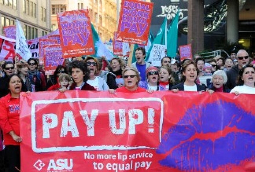 Protesters display banners for equal pay.