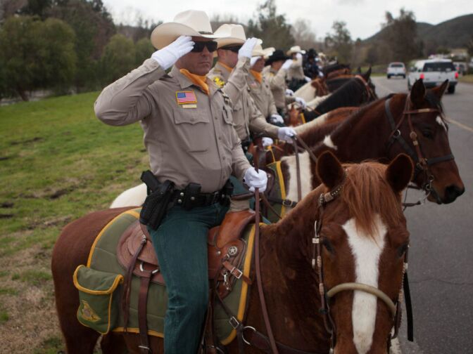 Mounted sheriff's deputies salute a passing motorcade for Det. Jeremiah MacKay in San Bernardino on Feb. 21, 2013.