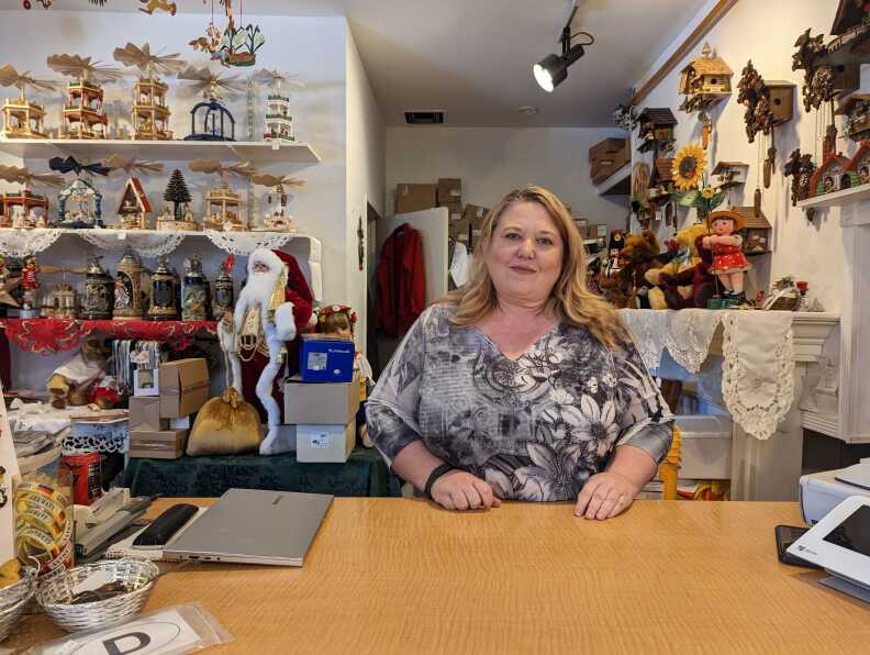 A light-toned woman stands behind a counter inside a toy store.