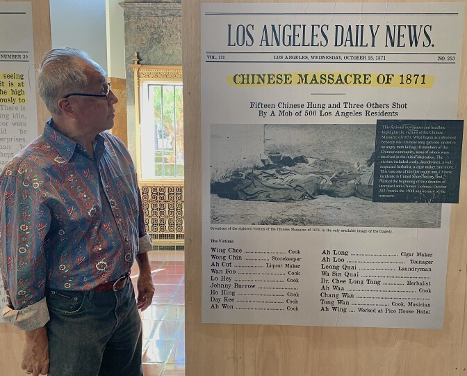 A 70-year-old Chinese American man stands in Union Station looking at an enlarged, fictionalized reproduction of a newspaper front page with the headline "Chinese Massacre of 1871: Fifteen Chinese Hung and Three Others Shot By A Mob of 500 Los Angeles Residents."
