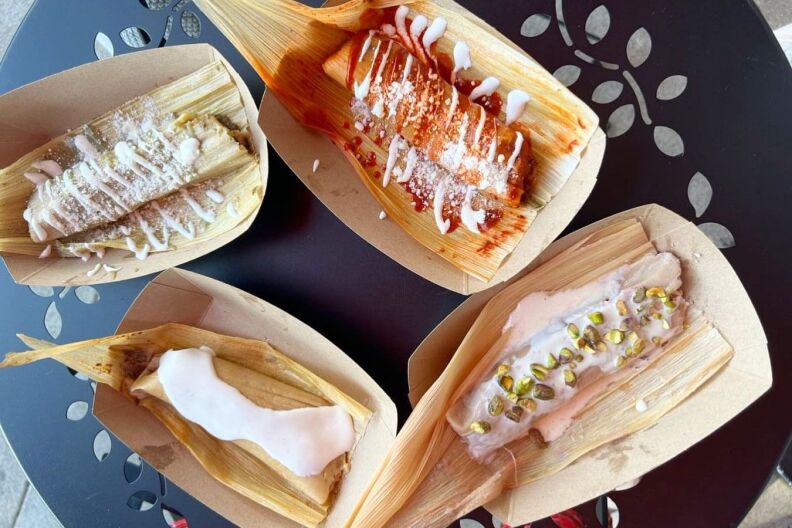 Four fresh tamales with various sauces and cheeses layered on top.