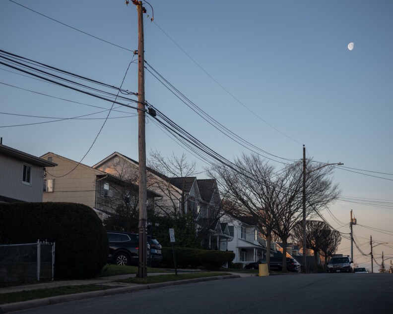 A residential street is lined with homes and phone and electrical poles and wires.