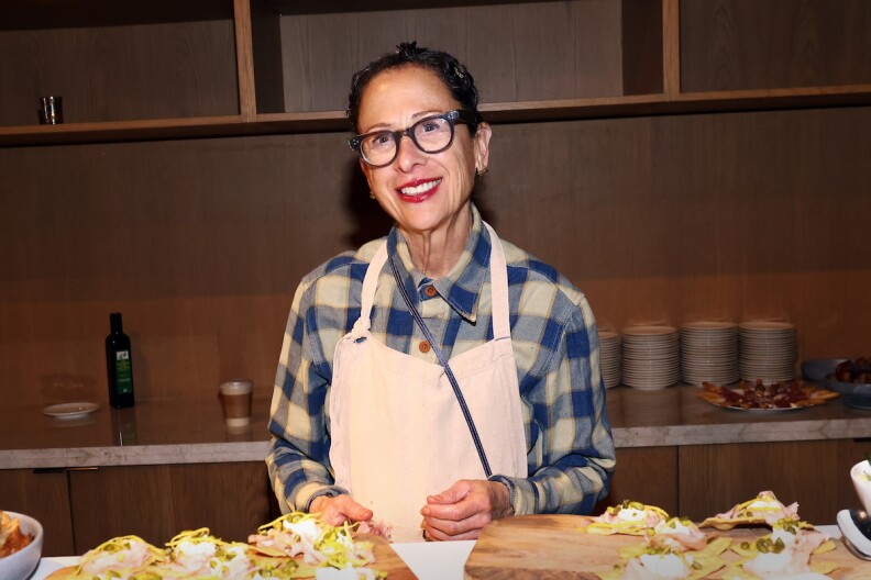 Chef Nancy Silverton wears an apron with open-face toasts spread out before her on a table.