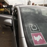 A passenger gets into a car marked as participating in both Uber and Lyft.
