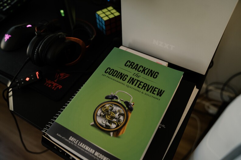 Headphones, a Rubik's Cube, and a book that reads "Cracking the Coding Interview" on the cover sit on a desk.