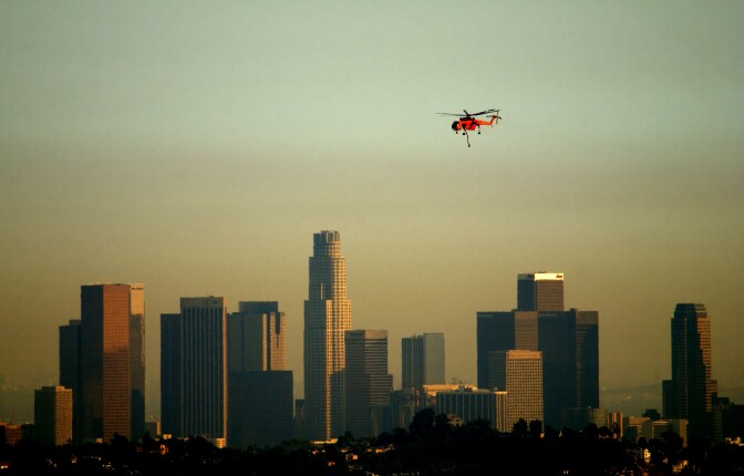 GLENDALE, CA - SEPTEMBER 9:  An Erickson Aircrane firefighting helicopter flies past a slightly smokey downtown Los Angeles skyline as it returns from picking water at an inner-city lake while fighting a wildfire September 9, 2002 in Glendale, California. Homes were threatened today but none were lost in the 800-plus acre wildfire burning in the Los Angeles suburbs of Glendale and Burbank. Containment of the fire is set at 20 percent. (Photo by David McNew/Getty Images)
