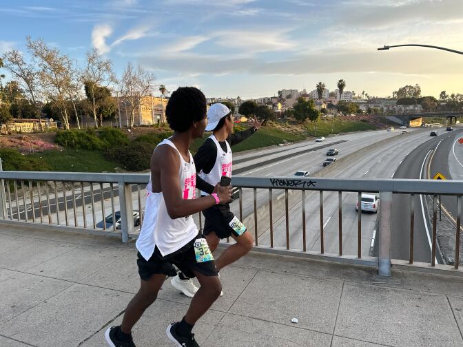 Two runners on the overpass looking down at the 101 Freeway.