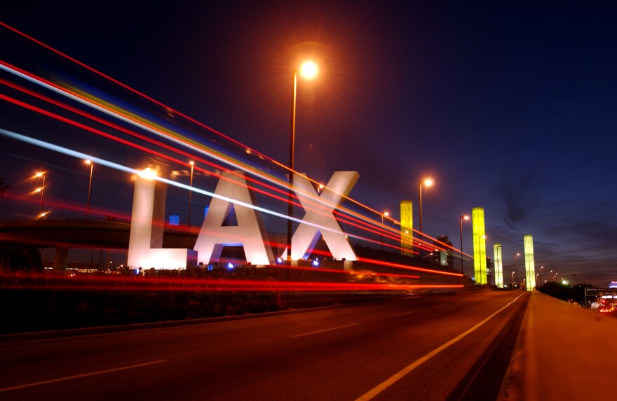 Four pillars lighted in yellow make the backdrop to a lighted LAX sign in giant letters.