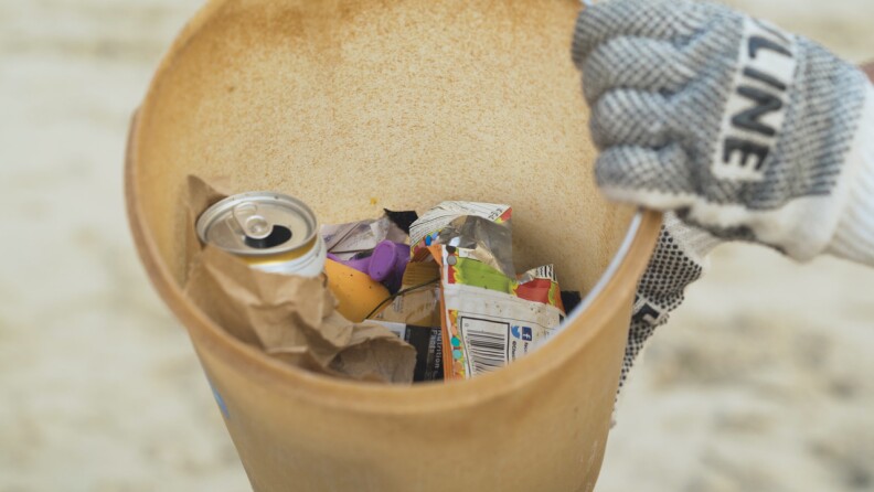 A bucket of trash collected by volunteers during California Coastal Cleanup Day includes with a soda can and a chip bag.