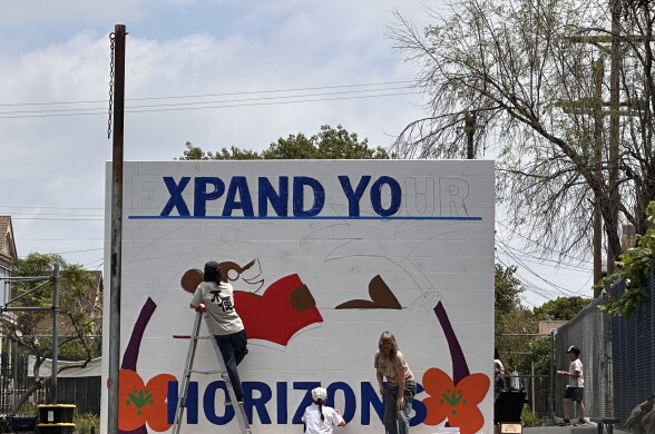 Three people painting a mural with a white background.