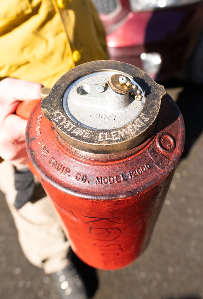 A red metal can being held by a person in a yellow coat.