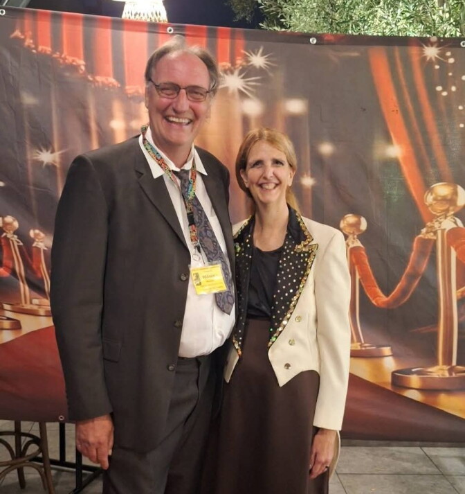 Two people smile together on a red carpet in front of a backdrop styled like an awards show entrance.