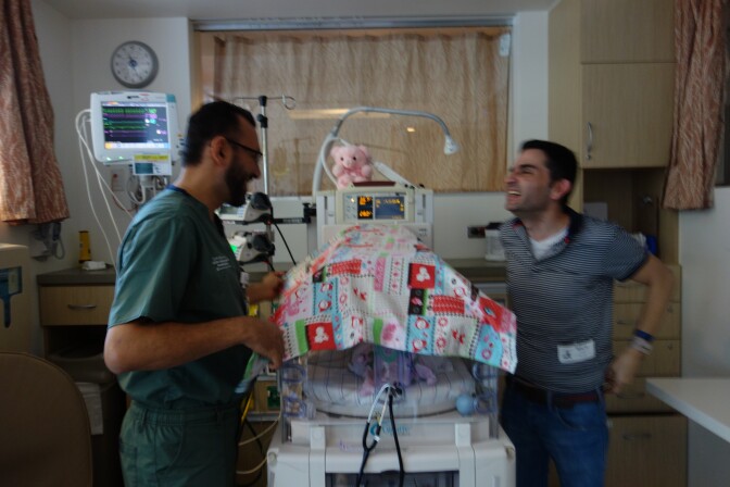 Dr. Antoine Soliman, medical director of the Miller Children's Hospital neonatal intensive care unit with new father Saturnino Izquierdo and baby Francesca in the Isolette under the blanket.