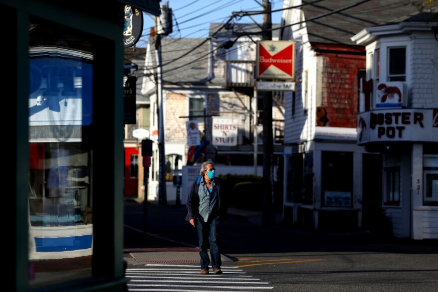 A man in a blue mask walks down a street lined with restaurants, bars and T-shirt stores.